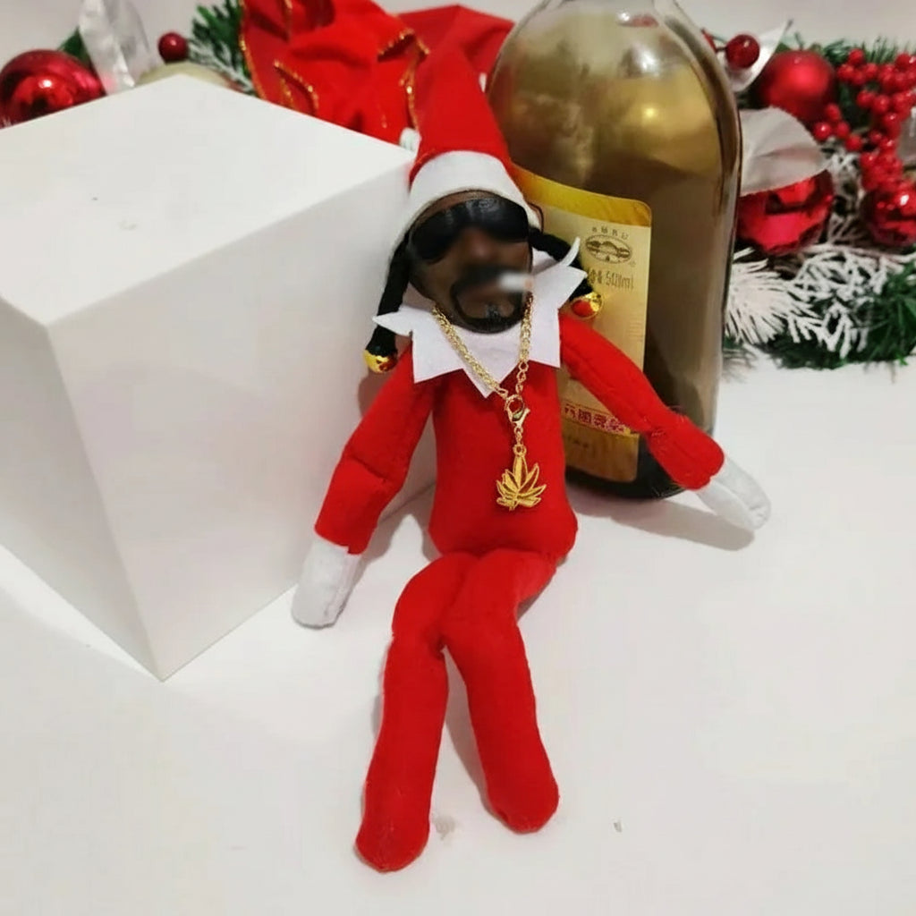 Elf doll with gold chain and red outfit next to a bottle of alcohol on a white surface.