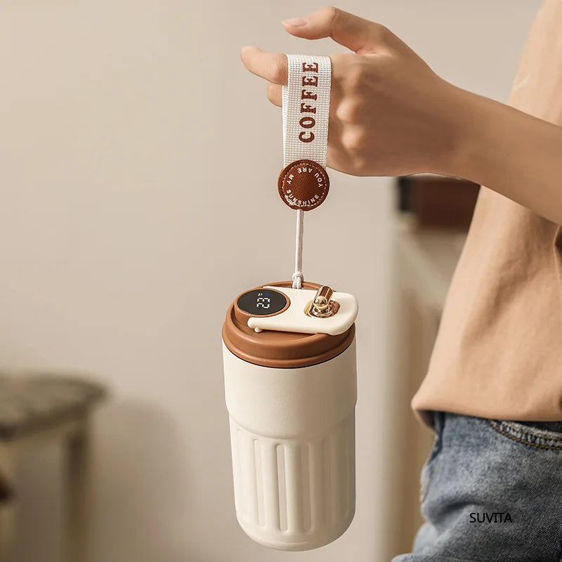 Hand holding a portable coffee maker with a brown lid and white body, featuring a &
