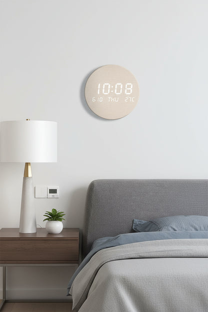 Round digital wall clock on a gray wall with a lamp and sofa in the background